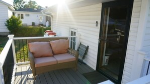 A covered porch with a wicker sofa and cushions, a glass door, and a white railing.