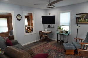 A living room with a ceiling fan, a flat-screen TV, a dining table with chairs, a sofa, and a patterned rug.
