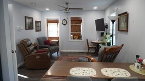 A living room with a sofa, a recliner, a dining table with placemats, a TV, and a ceiling fan.