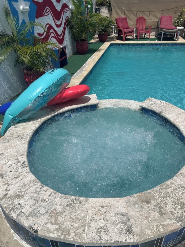 A swimming pool with a hot tub, lounge chairs, and potted plants.