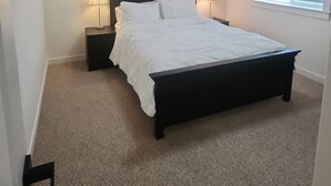 A bedroom with a bed, two bedside tables with lamps, a ceiling light, and a window with blinds.