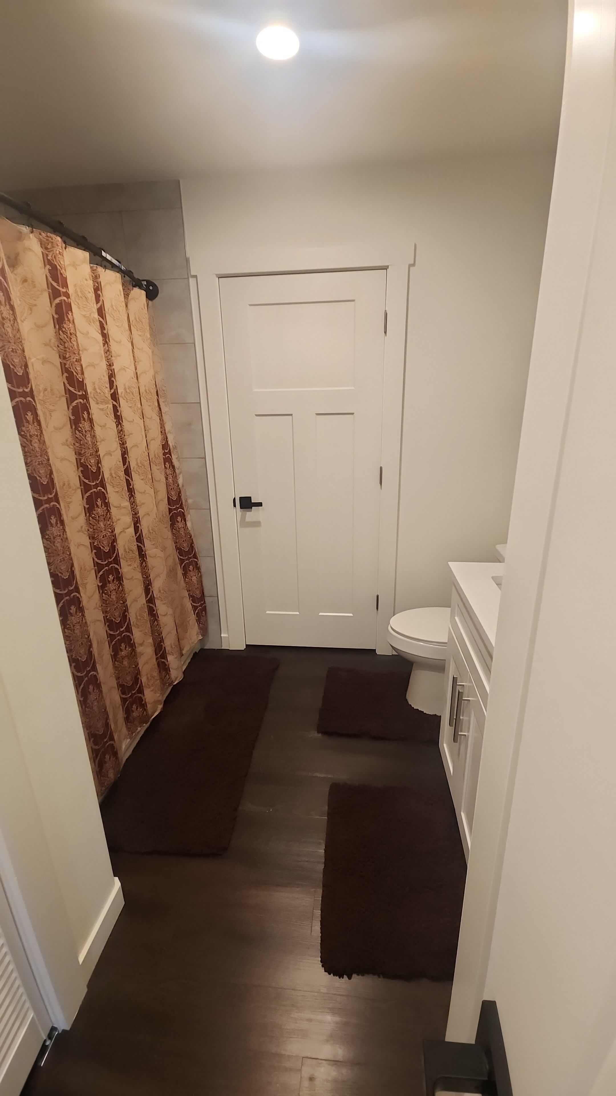 A bathroom with a white door, a toilet, a sink, and a shower curtain.