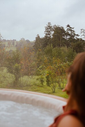 Una persona con remera roja sentada en un jacuzzi con vista a un paisaje boscoso.