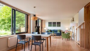 A modern living room with a dining area, large windows, and a view of greenery.