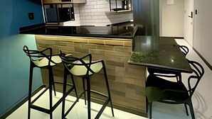 A modern kitchen with a central island, bar stools, and a dining table. - LOFT JANELAS DO CARIBE - 315 (Arraial do Cabo)