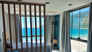 A modern hotel room with a large bed, a blue sofa, and a view of the ocean. - LOFT JANELAS DO CARIBE - 315 (Arraial do Cabo)