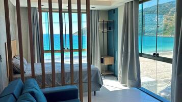 A modern bedroom with a large bed, a sofa, a view of the sea, and a balcony with curtains.