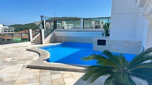 A rooftop swimming pool with a glass balustrade, a palm tree, and a view of the surrounding buildings. - LOFT JANELAS DO CARIBE - 315 (Arraial do Cabo)