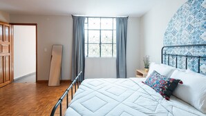 Een slaapkamer met een bed, een raam met gordijnen, een houten vloer en een hoofdeinde met een patroon.