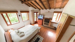 Un dormitorio acogedor con techo de madera, una cama con colcha blanca, un televisor y una chimenea.