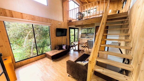 Amplia sala de estar con escalera de madera, ventanas grandes y un rincón de estar acogedor.