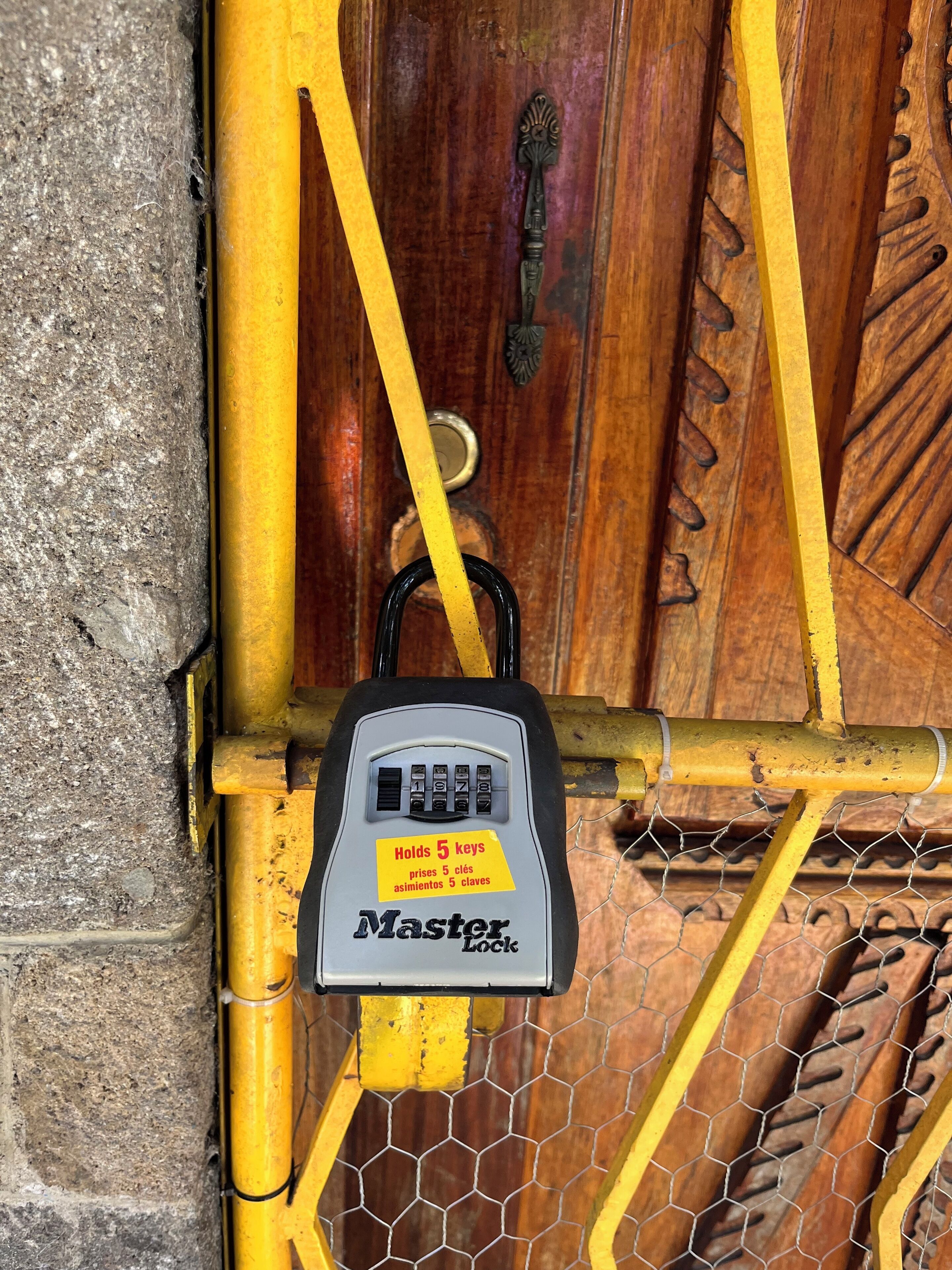 A Master Lock padlock attached to a yellow metal gate with a wooden door in the background.