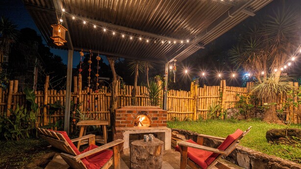 Eine Terrassenausstattung im Freien mit Feuerstelle aus Ziegeln, Holzstühlen und einem Bambuszaun.