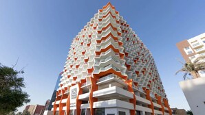 A modern hotel with a distinctive zigzag facade, multiple balconies, and a clear sky in the background.