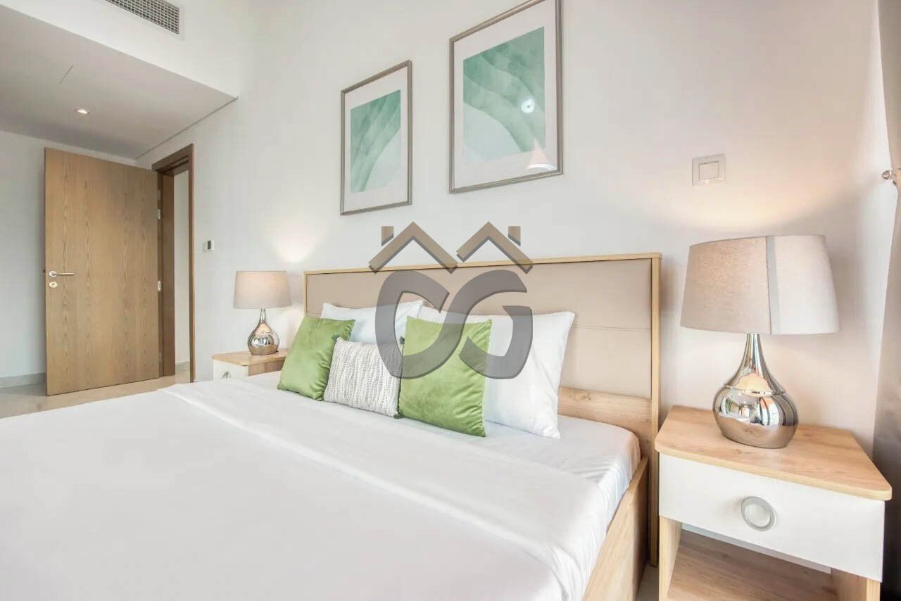 Une chambre d’hôtel avec un grand lit, deux tables de chevet, une porte en bois et deux tableaux encadrés au mur.