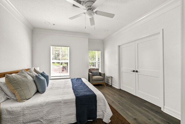 A bedroom with a bed, a ceiling fan, a chair, and a door.