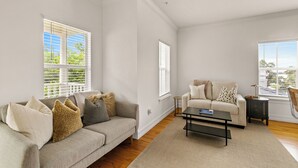 A living room with a beige sofa, a coffee table, and a window with blinds. - Beautiful Townhouse IN THE VERY HEART OF DT MT, DORA! (Mount Dora)
