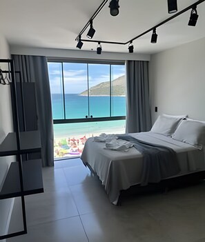 A modern bedroom with a large bed, a desk, and a balcony with a view of the sea. - LOFT PARADISO - 411 (Arraial do Cabo)