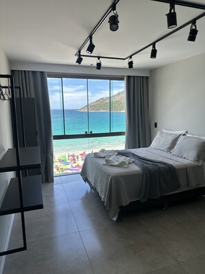 A bedroom with a large bed, a TV, and a view of the beach. - LOFT PARADISO - 411 (Arraial do Cabo)