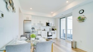 Una cocina moderna con armarios blancos, un refrigerador de acero inoxidable y un microondas. Hay una mesa de comedor con sillas y una planta en maceta.