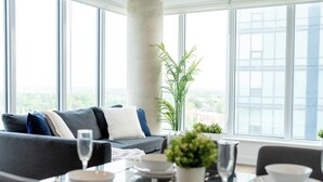 Una sala moderna con sofá, mesa de comedor y ventanas amplias que ofrecen vistas de la ciudad.