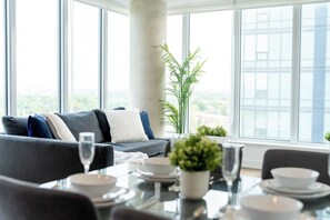 Ein modernes Wohnzimmer mit Sofa, Esstisch und großen Fenstern mit Blick auf die Stadt.