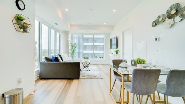 Una sala de estar moderna con un sofá, una mesa de comedor y sillas. Hay un ventanal que proporciona luz natural y vistas de la ciudad.