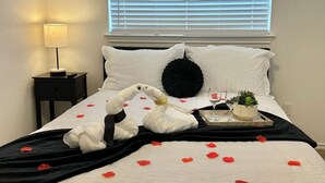 Un lit bien fait, avec une couette noire et blanche, une lampe de chevet et un plateau sur lequel se trouvent un verre d’eau et une petite plante.