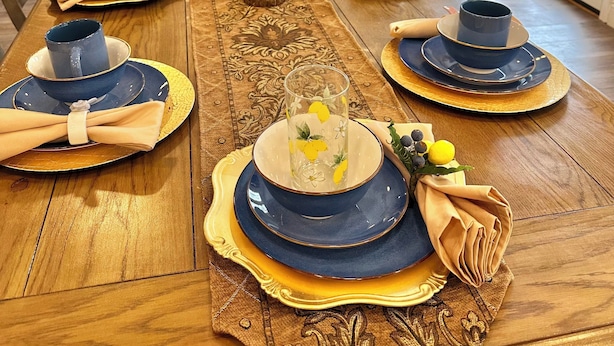 Une table à manger dressée avec de l’argenterie bleue et dorée, des serviettes et un grand vase.