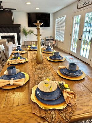 Una mesa de comedor dispuesta con platos azules y dorados, servilletas y un jarrón alto.