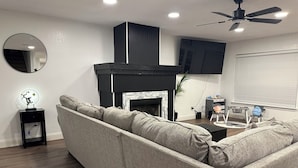 Un salon comprenant un canapé d’angle, une cheminée, un ventilateur de plafond et un téléviseur fixé au mur.
