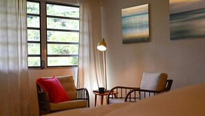 Une pièce comprenant un lit, un canapé avec un coussin rouge, une chaise, une petite table avec une tasse et un lampadaire.