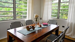 Une table à manger avec des chaises, un vase rempli de fleurs, une bouteille d’eau et une assiette avec de la nourriture.
