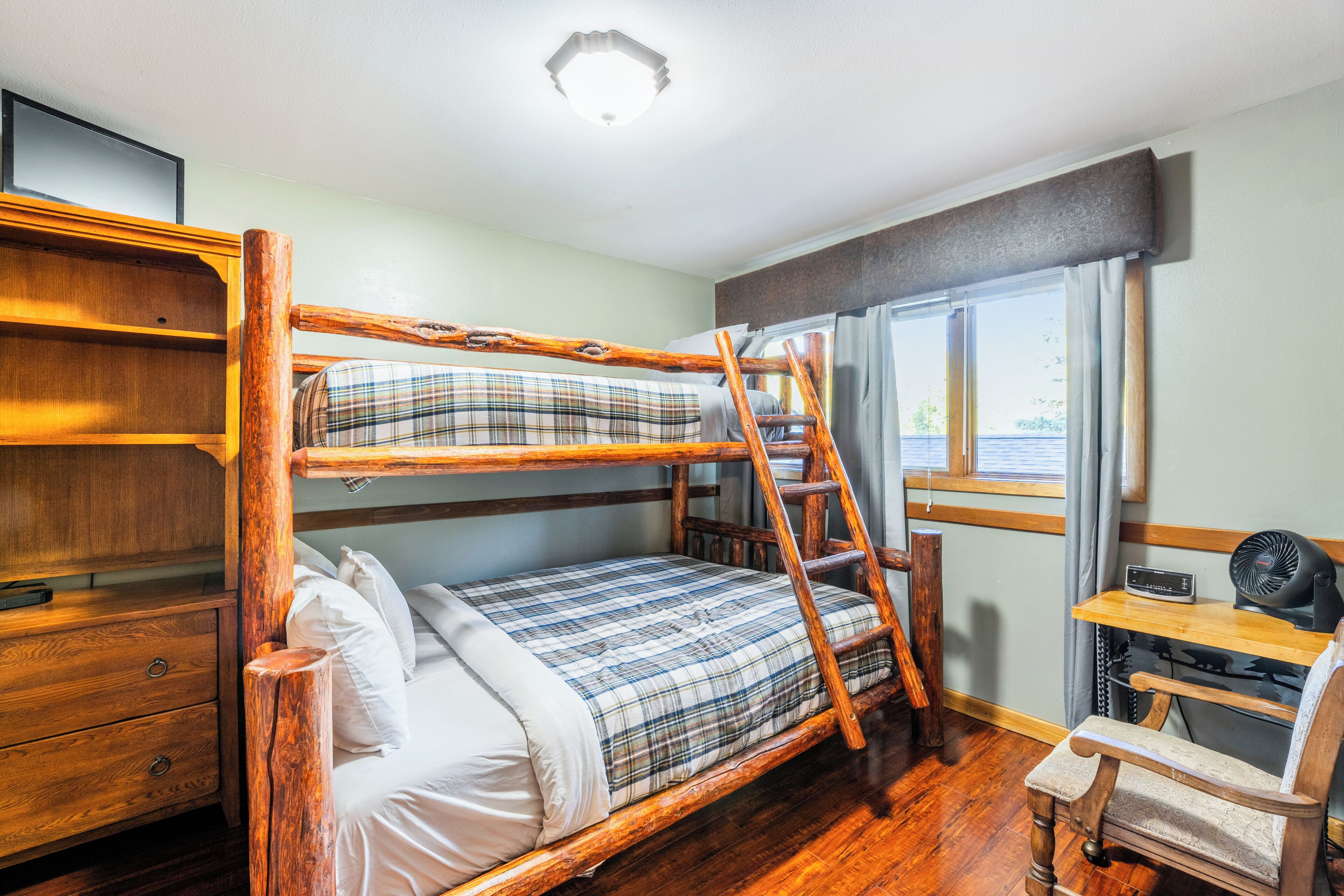 Ein Stockbett mit einer Stehleiter, ein Holztisch und ein Stuhl in einem Zimmer mit Holzboden und einem Fenster.
