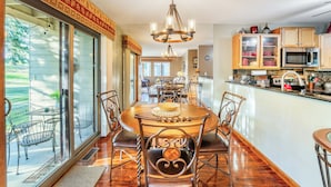 A dining area with a large wooden table and chairs, a chandelier, and a view of the outdoors.