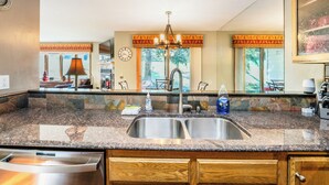 A kitchen with granite countertops, stainless steel sink, wooden cabinets, and a chandelier.