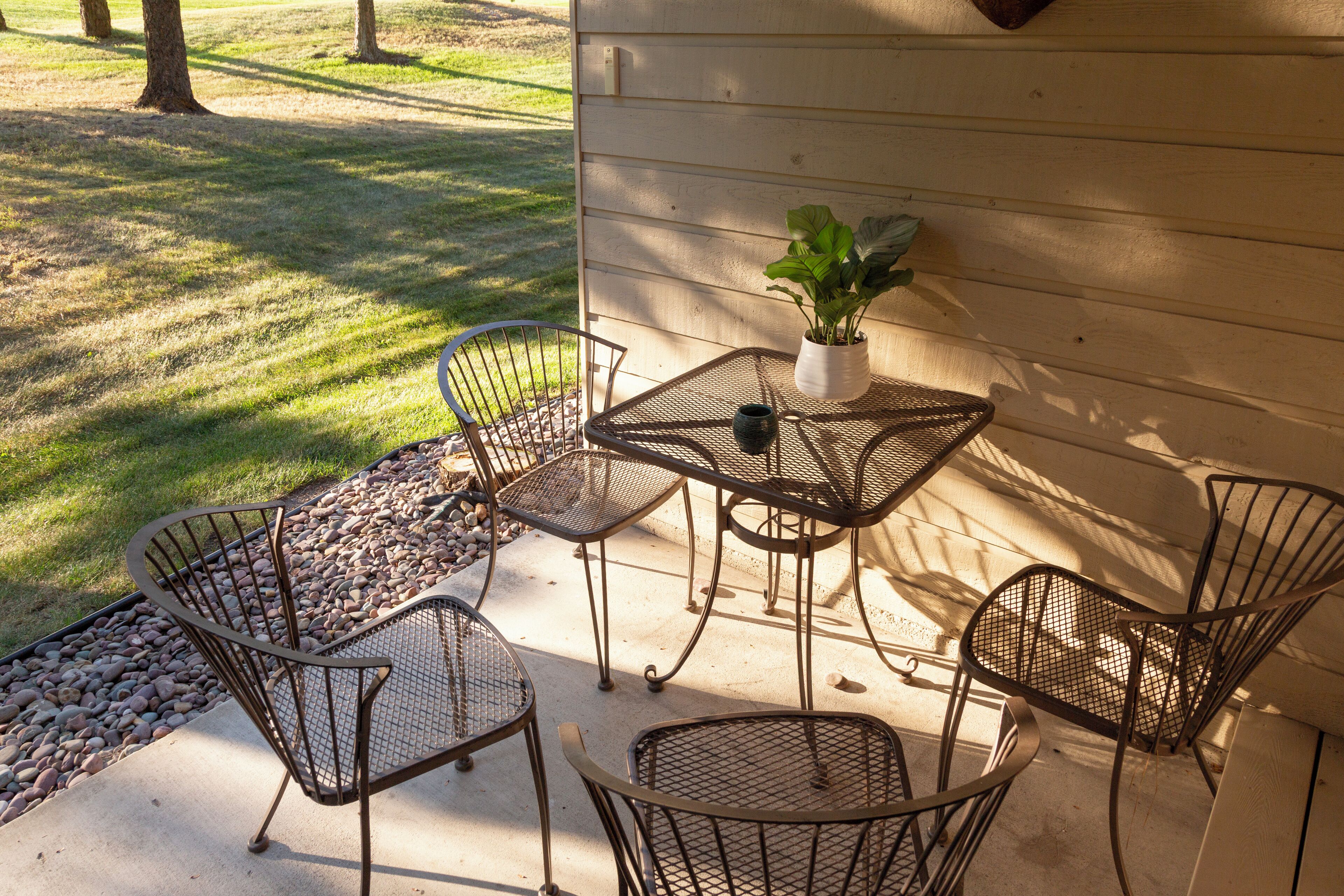 En terrasse med metalstole og et bord, en potteplante og en stensti.