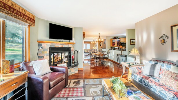 A spacious living room with a fireplace, leather sofas, a television, and a dining area in the background.