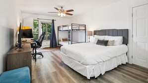 Un dormitorio con literas, un escritorio con computadora, una silla, un ventilador de techo y una ventana con cortinas.