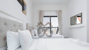 A hotel room with a large bed, a window with curtains, a mounted TV, and a view of the city.