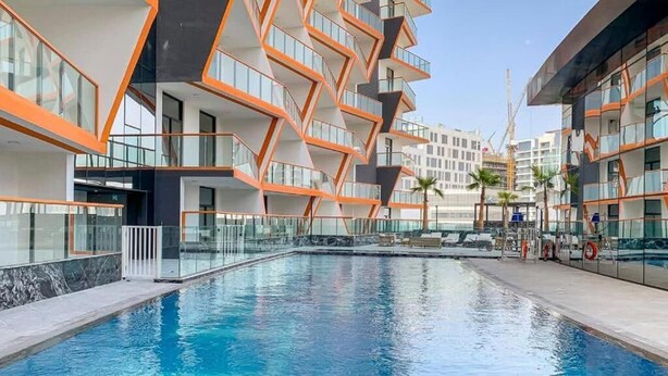 A modern hotel with a central swimming pool, multiple balconies, and a view of the surrounding area.