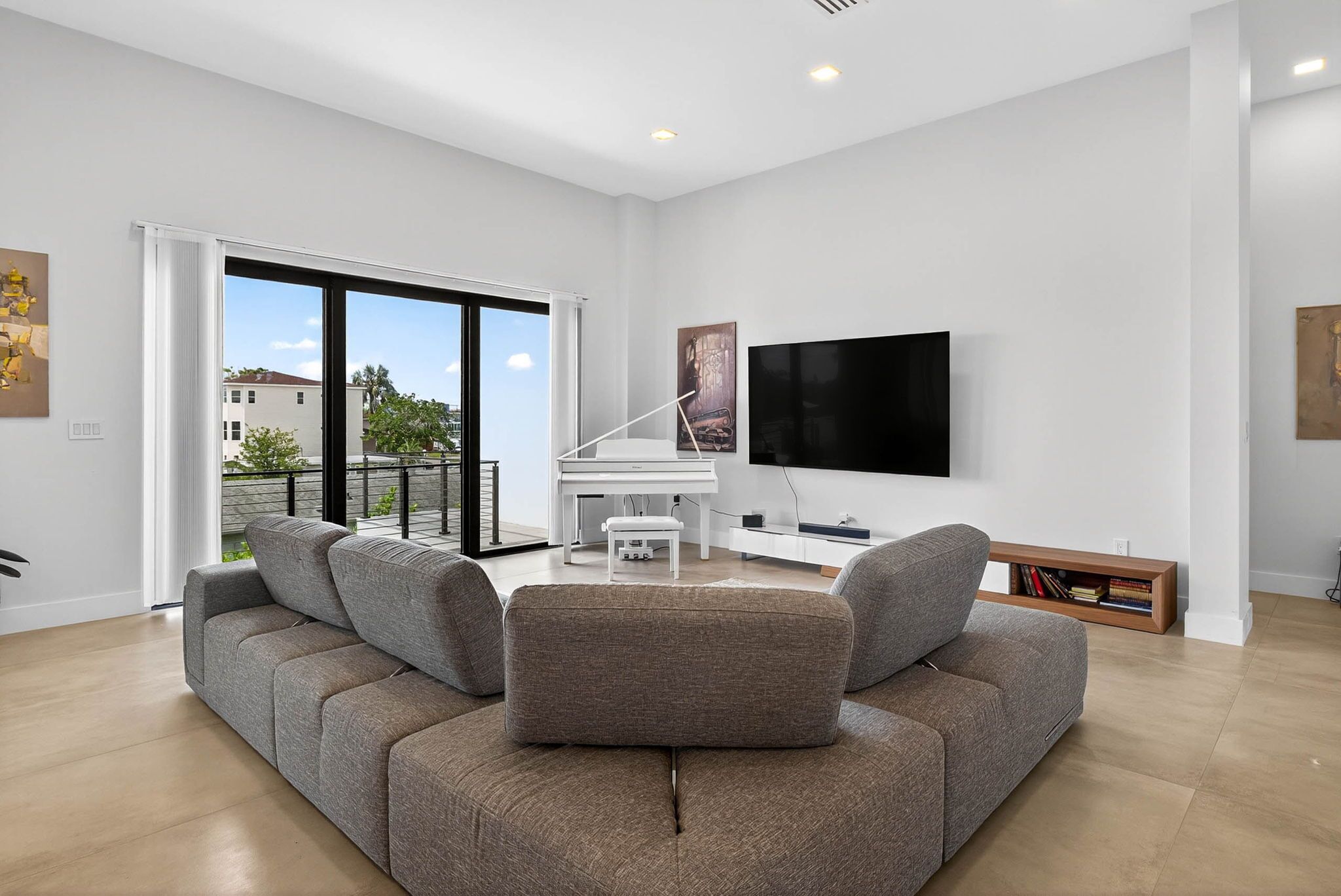 Ein modernes Wohnzimmer mit einem grauen Ecksofa, einem weißen Klavier und einem Flachbildfernseher an der Wand.