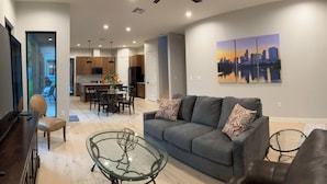 A modern living room with a grey sofa, a glass coffee table, and a cityscape painting on the wall.