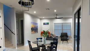 A modern kitchen with a marble countertop, dining area with chairs and a vase of flowers, a black leather sofa, and a ceiling fan.