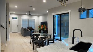 A modern kitchen with a marble countertop, black sink, and dining area with chairs and a glass table.