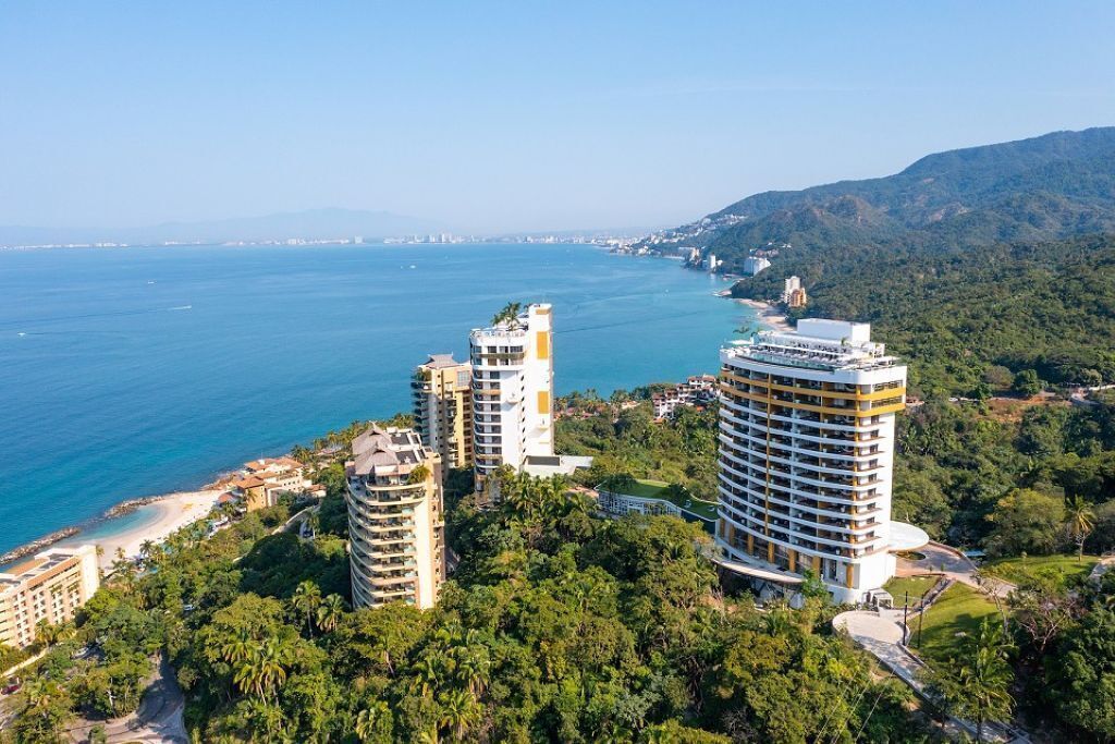 Un hôtel situé sur la côte, composé de plusieurs immeubles de grande hauteur, doté d’une plage et entouré d’une végétation luxuriante.