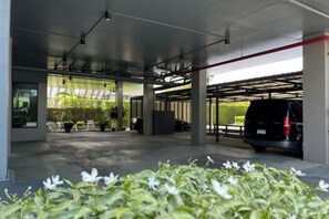 Un espace de stationnement couvert avec un véhicule, des colonnes et une vue sur la verdure à l'extérieur.