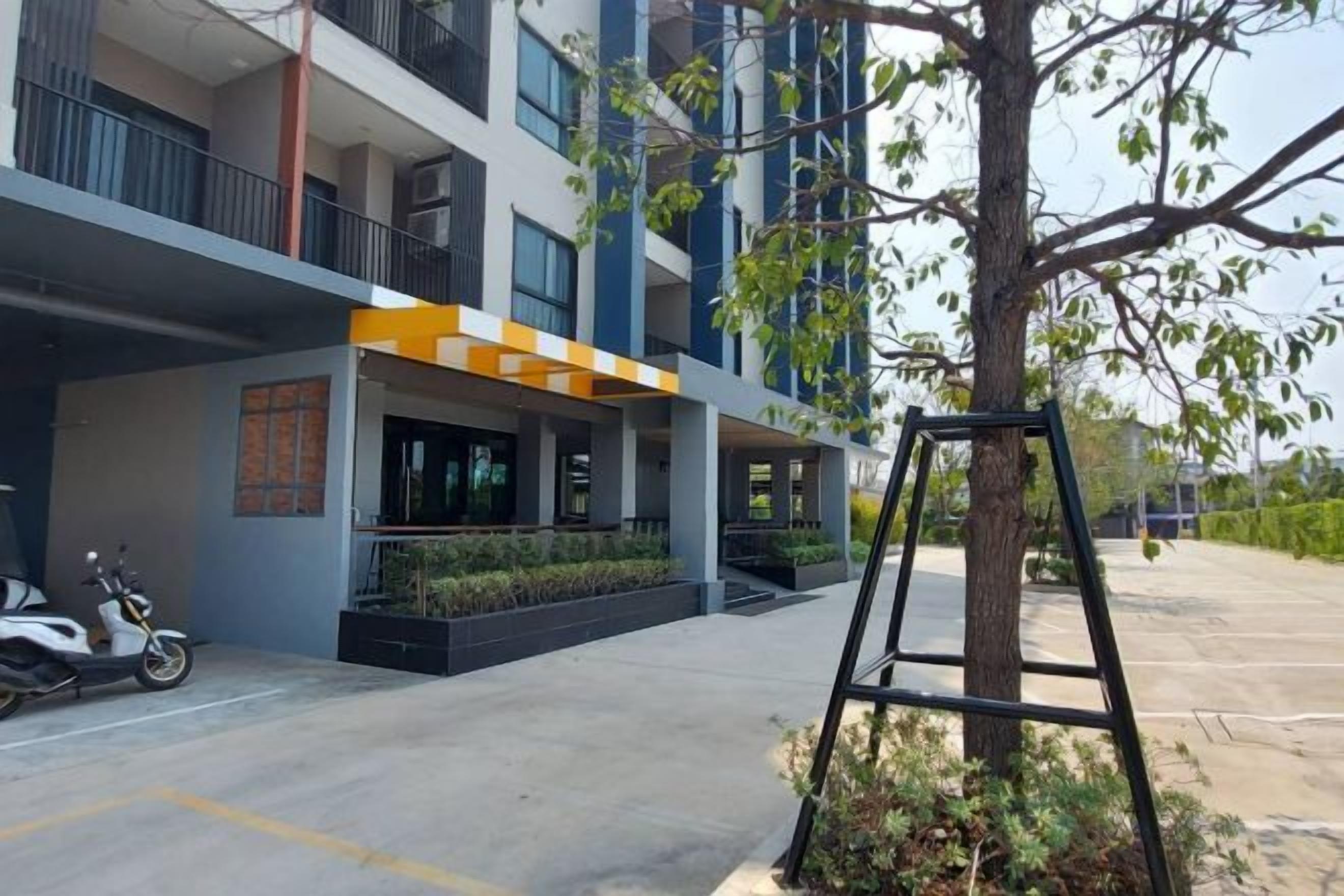 Un edificio moderno con un acceso cubierto, un árbol y una moto estacionada.