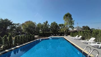 A swimming pool with a clear blue water surface, surrounded by trees and a row of white lounge chairs.