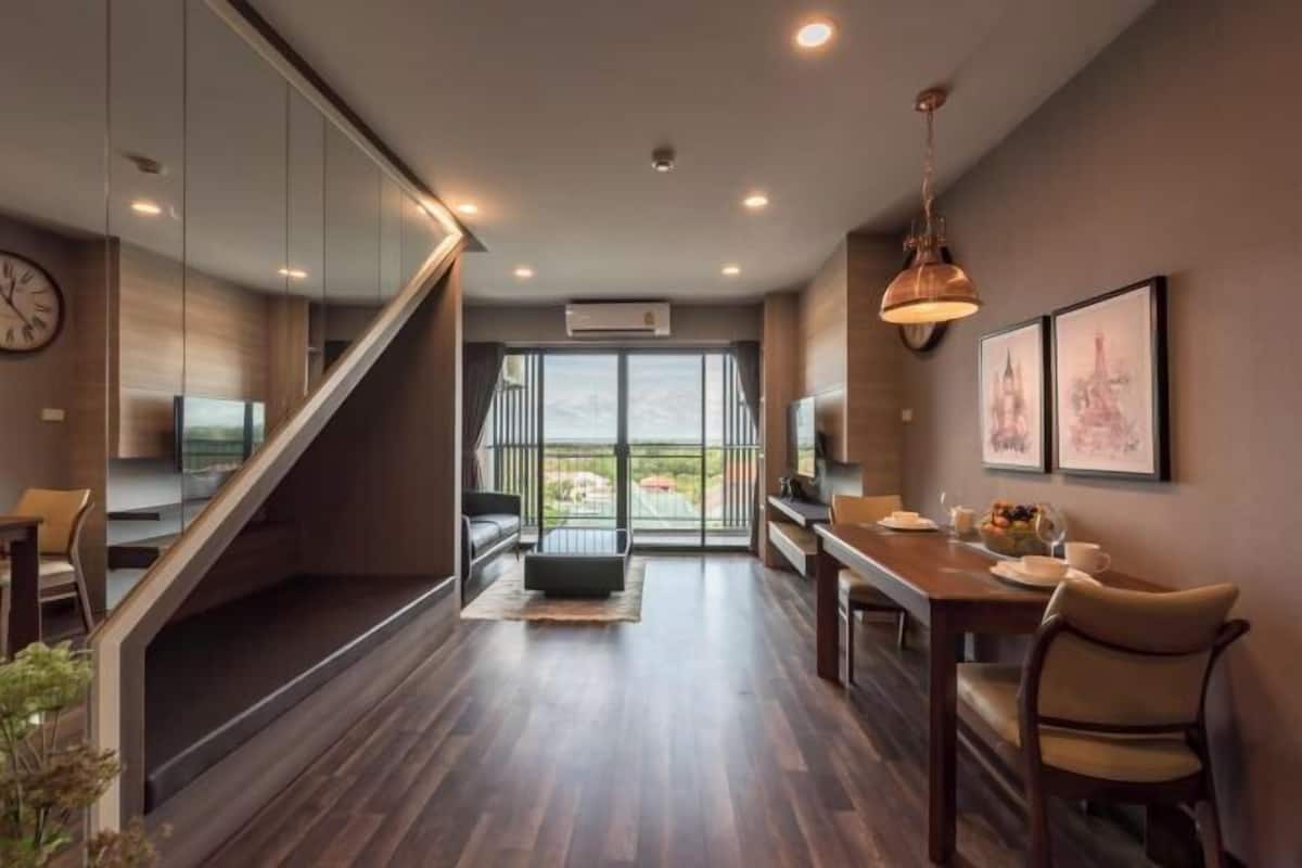 Une chambre d’hôtel moderne avec un plancher en bois, un escalier, un coin repas et une grande fenêtre donnant sur un beau paysage.
